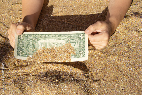 Canvas Print Children's hands pull a bill of one dollar from the sea sand