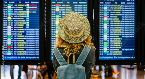 portrait and close up of the back of curly woman checking the time of her flight in the airport to traveling outdoors and enjoy her vacations - noamd lifestyle and concept photo