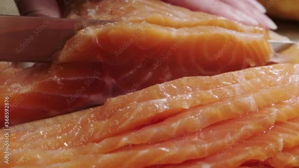 A woman's hand cuts fresh salmon by slices. close-up cutting board with red fish on the table. A woman's hand cuts fresh salmon by slices. close-up cutting board with red fish on the table.