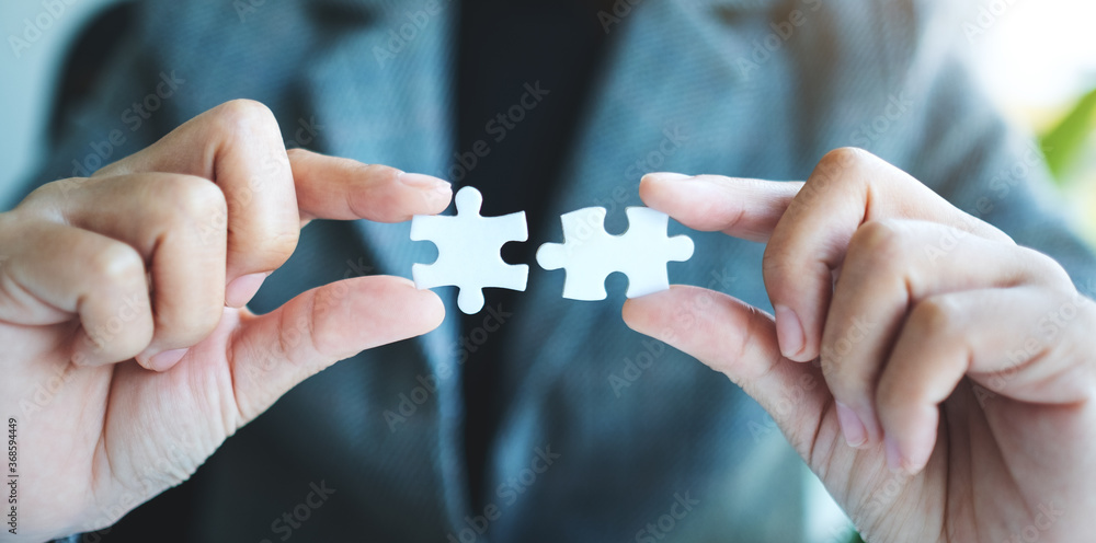 Closeup image of a businesswoman holding and putting a piece of white jigsaw puzzle together