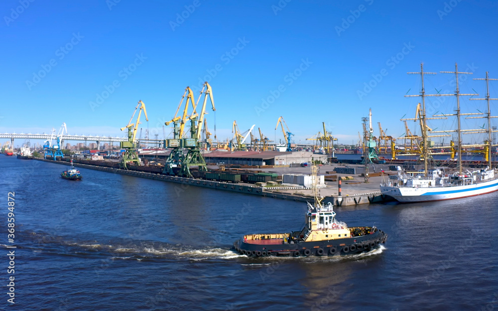 Aerial view of a row of construction or cargo cranes on the banks of a river with a boat sailing nearby.