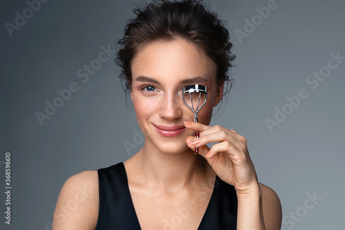 Obraz na plátně Beautiful woman using eyelash curler on long eyelashes