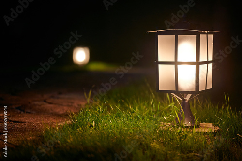 Illuminated garden alley in the night. lantern on hook illuminating the board of the yard