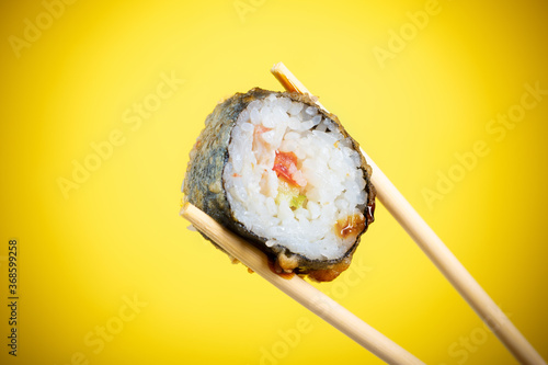 Sushi rolls close-up in wooden sticks on a bright yellow gradient background
