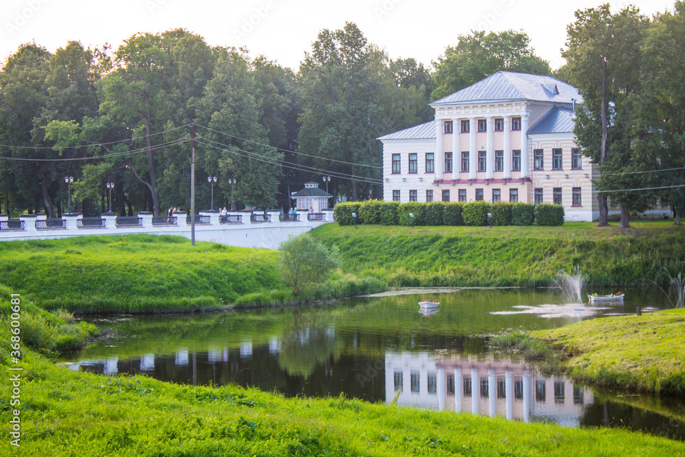 the former city Duma Building in a Park among green trees with reflection in the pond against a blue sky and a space for copying on a summer day Uglich Russia