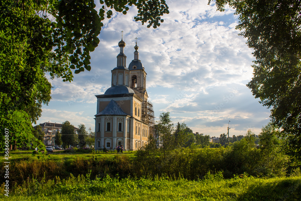yellow Church of the Kazan icon of the mother of God among green trees against a cloudy sky and space for copying in Uglich Russia