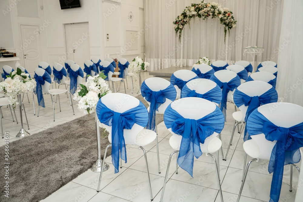Bright room for weddings. Rows of guest chairs decorated with blue cloth Bright room for weddings. Rows of guest chairs decorated with blue cloth