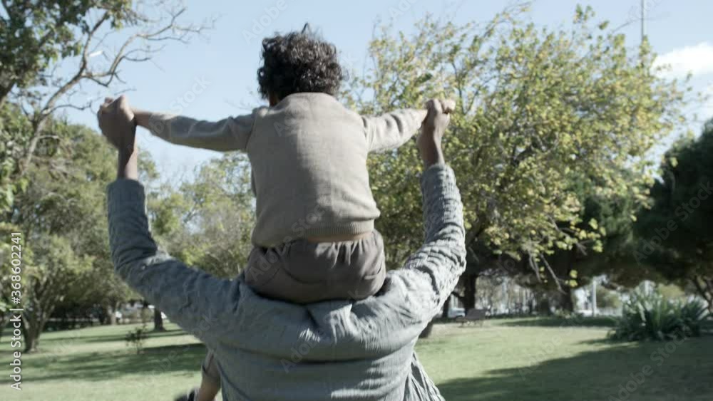 African American father holding son on shoulders, spreading hands and