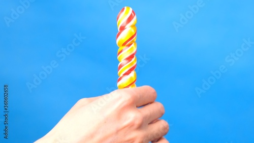 Close up of female hands. In a female hand a candy lollipop, on the other hand, a woman imitates masturbation. Blue simple background.