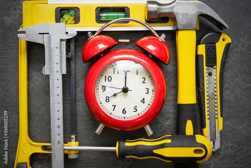 Red alarm clock and work tools on the table. Repair time abstract background.