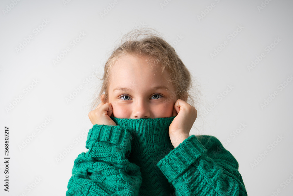charming little girl hides her lower face under the thick collar of a warm knitted sweater. Children, gestures and emotions, happiness, winter. Close up studio shot isolated on white, copy space charming little girl hides her lower face under the thick collar of a warm knitted sweater. Children, gestures and emotions, happiness, winter. Close up studio shot isolated on white, copy space