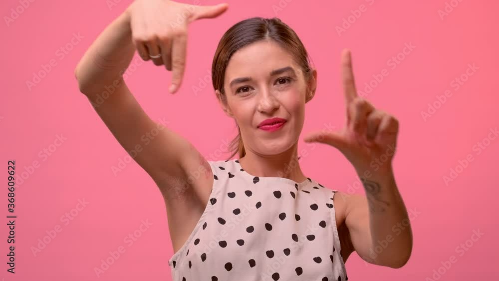 Close up portrait of smiling lovely shiny European girl through the frame of her hands in front of the camera. Woman in a cheerful high spirits, making fun posing on a pink studio background. Close up portrait of smiling lovely shiny European girl through the frame of her hands in front of the camera. Woman in a cheerful high spirits, making fun posing on a pink studio background.