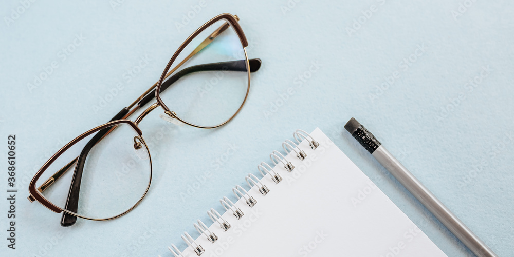 Office concept. Workspace with glasses, notebook and pencil. Copy space white and blue background. Office concept. Workspace with glasses, notebook and pencil. Copy space white and blue background.