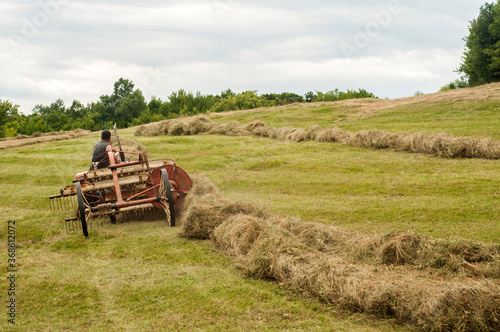 Collecting hay by vintage mashines on mountain meadow in summertime photo