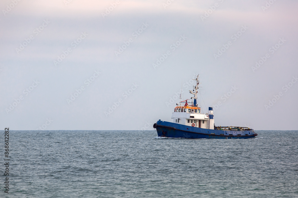 towing ship in the open sea, blue tugboat sailing on sea water against the sky.