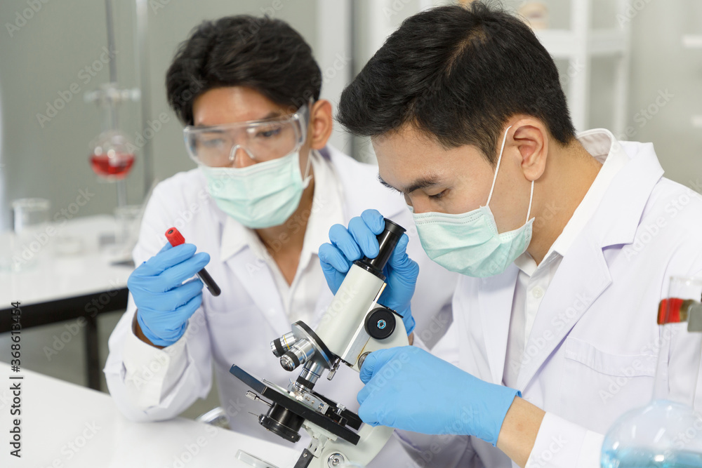 Two Male Scientists wear Face Mask working in Lab while Checking Blood tested by micro scope. SARS-CoV-2 , Covid-19 THEME. Two Male Scientists wear Face Mask working in Lab while Checking Blood tested by micro scope. SARS-CoV-2 , Covid-19 THEME.