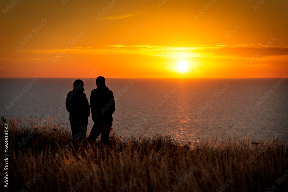 Paar blickt in den Sonnenuntergang auf einer Steilküste am Meer