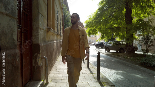 Front view of adult male traveler in yellow shirt walks along a narrow old street. Tourism during quarantine © Honchar