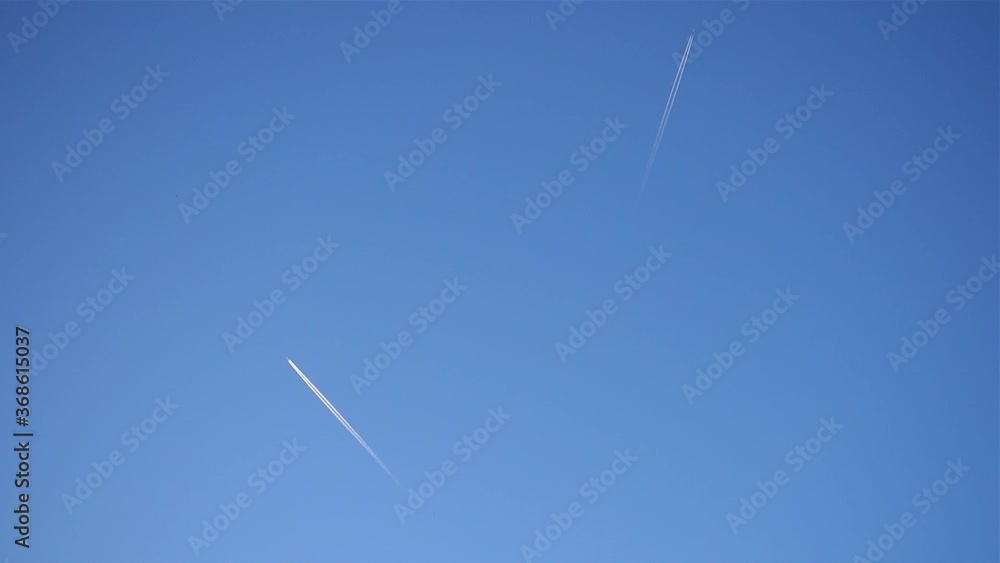 Airplane trails across clear blue sky, slow motion. Two large passenger supersonic planes flying high in clear blue sky, leaving long white trails. Transportation and travel concept.