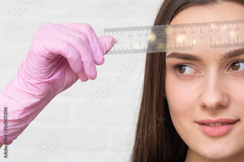 Young girl with a ruler to adjust the shape of the eyebrows, Spa or beauty salon,