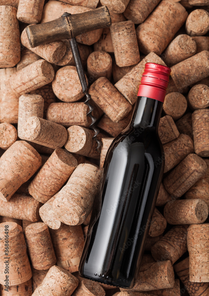 Bottle of red wine and vintage corkscrew on top of various wine corks.