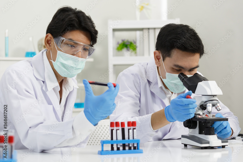 Two Male Scientists wear Face Mask working in Lab while Checking Blood tested by micro scope. SARS-CoV-2 , Covid-19 THEME. Two Male Scientists wear Face Mask working in Lab while Checking Blood tested by micro scope. SARS-CoV-2 , Covid-19 THEME.