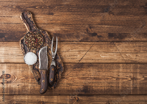 Vintage fork and knife for meat on wooden chopping board with salt and pepper on wooden table background. Space for text
