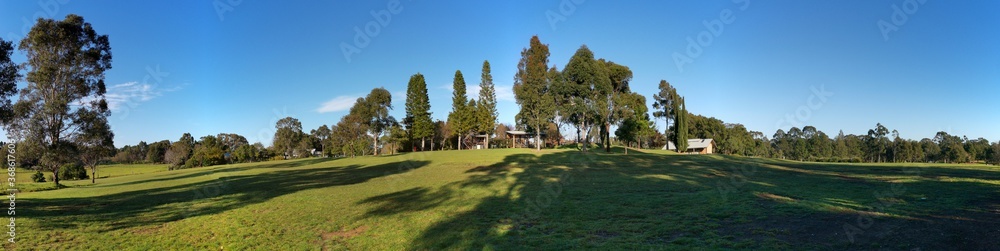 Beautiful morning panoramic view of a park with green grass, tall trees and blue puffy sky, Fagan park, Galston, Sydney, New South Wales, Australia