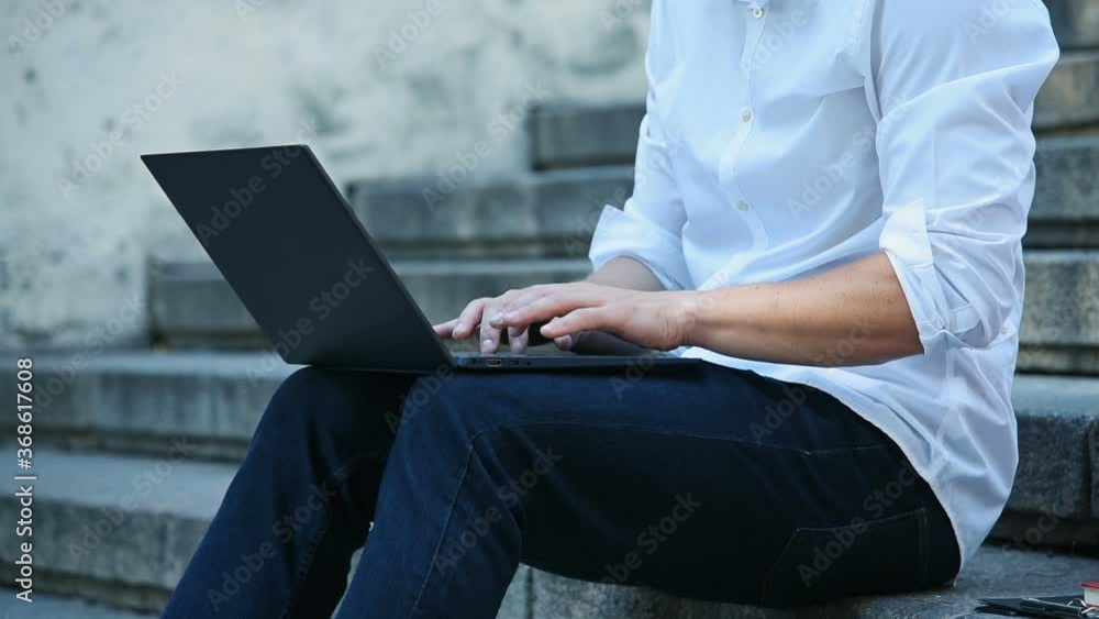 Young Businessman Sitting On Stairs And Typing On Keyboard Laptop. Business And Education Concept. Slow Motion Effect. Young Businessman Sitting On Stairs And Typing On Keyboard Laptop. Business And Education Concept. Slow Motion Effect.
