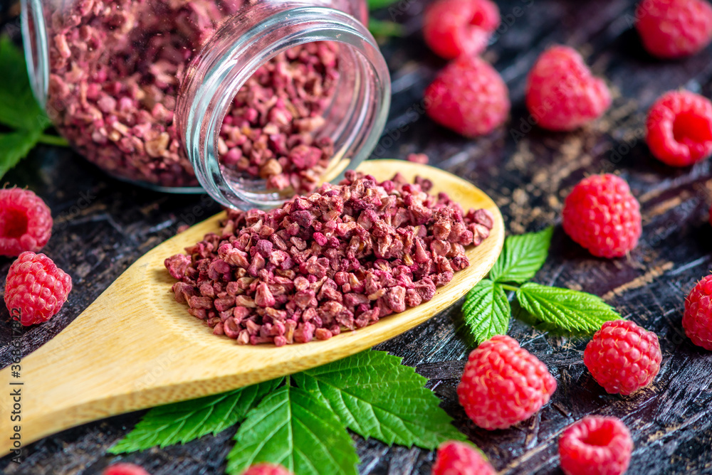 Freeze dried raspberries in a glass jar and a wooden spoon on a black background. Concept of berry storage types Freeze dried raspberries in a glass jar and a wooden spoon on a black background. Concept of berry storage types
