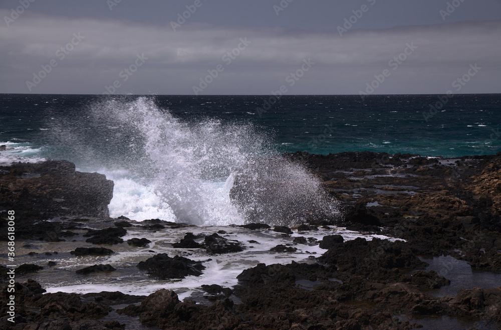 Gran Canaria, north west coast around natural swimming pools Salinas de Agaete, 
waves breaking against old eroded dark lava platform
