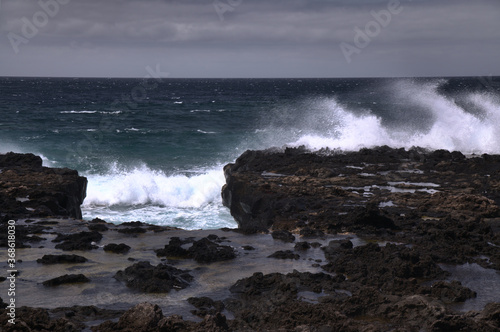 Gran Canaria, north west coast around natural swimming pools Salinas de Agaete, waves breaking against old eroded dark lava platform 