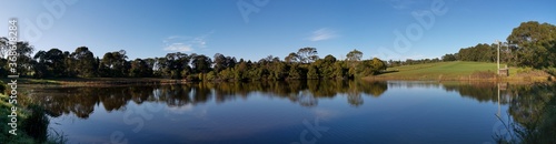 Beautiful morning panoramic view of a peaceful pond in a park with reflections of deep blue sky and tall trees, Fagan park, Galston, Sydney, New South Wales, Australia