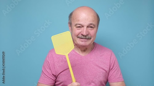man with fly swatter trying to kill mosquito on blue background.