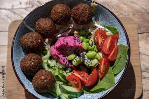 Bowl with falafel balls, hummus and fresh salad, wooden background top view