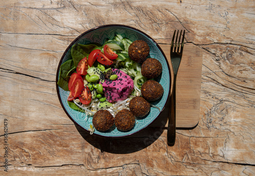 Bowl with falafel balls, hummus and fresh salad, wooden background top view