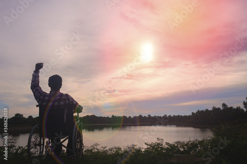 Silhouette young disabled man seeing river background.He is raise a hand to and sitting on wheelchair.despair,lonely,hope.Photo concept depression and Patient. © Teerayut