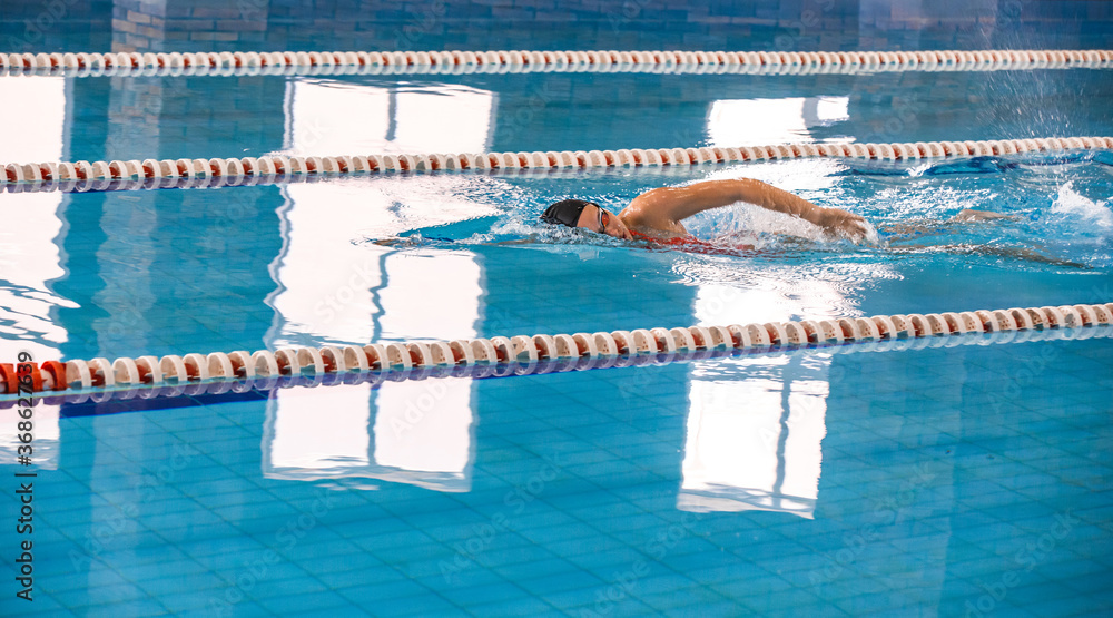 Young woman swimmer is swimming in the pool. Freestyle stroke, front crawl stroke. Swimming in blue pool, side view