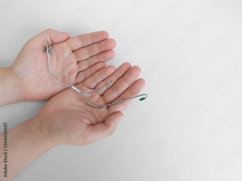 Closeup of teenager hands holding orthodontic device, removable metal braces for upper teeth,used together with dental rubber bands during braces,on white background. Selective focus.Copy space. Closeup of teenager hands holding orthodontic device, removable metal braces for upper teeth,used together with dental rubber bands during braces,on white background. Selective focus.Copy space.
