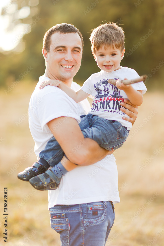 Fototapeta premium Family with children walking outdoors in summer field at sunset. Father and his little son having fun in summer field. People, family day and lifestyle concept