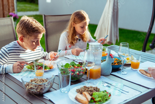 Happy family with two teen children eating healthy dinner together on terrace