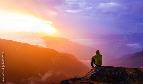 A lonely man sitting on top of a mountain and watching a beautiful and colorful sunset in Nepal. A trekker resting on top of a mountain in Langtang National park.