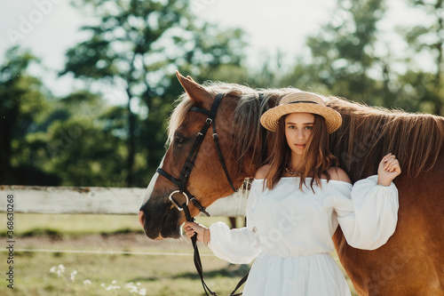 Beautiful hippie girl with horse on a ranch background, front view. The girl in the hat. Soft focus