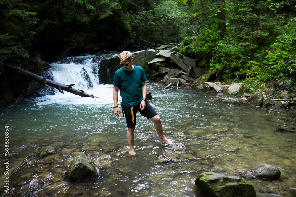 Young guy stands by the river against the background of a waterfall Young guy stands by the river against the background of a waterfall