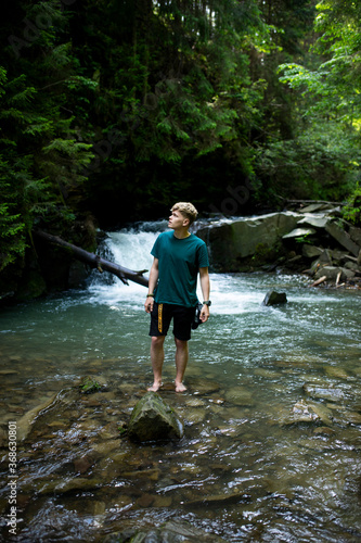 Young guy stands by the river against the background of a waterfall