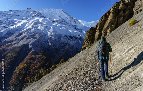 A male hiker walking on a narrow trekking trail in high altitude trail to Tilicho lake. A man walking towards the mountains in Nepal. photo