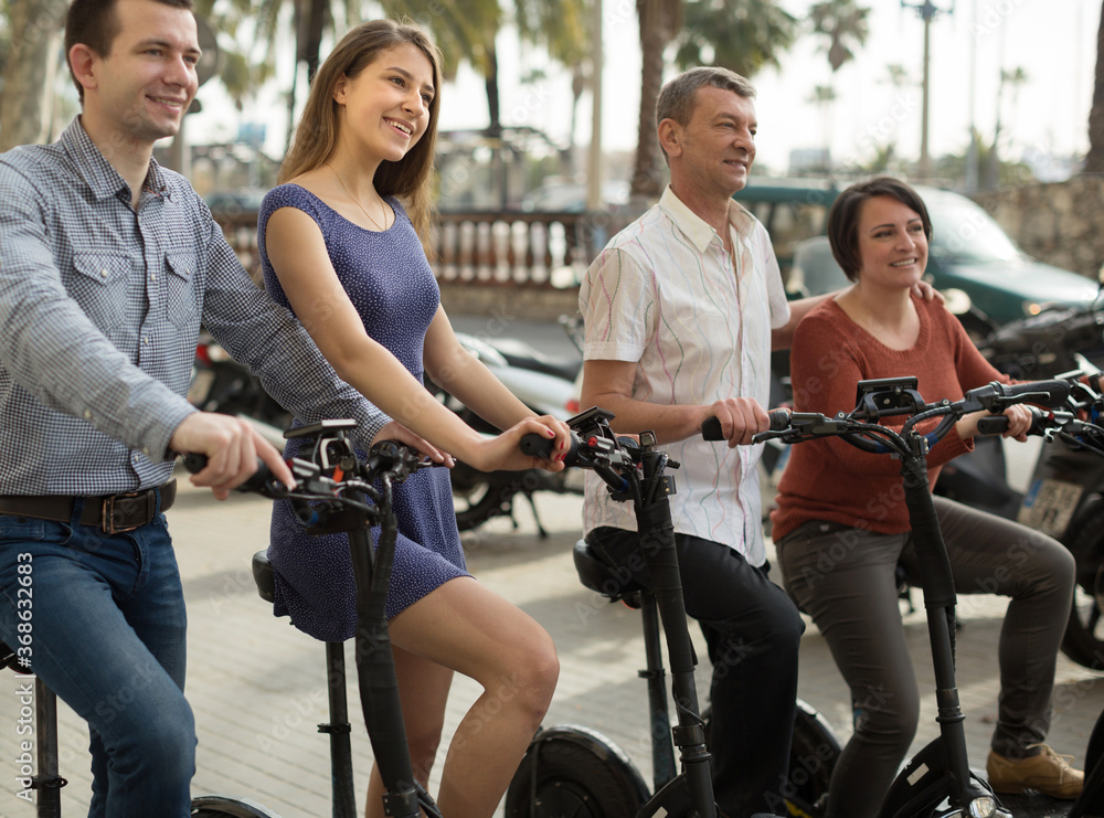 Obraz premium friends of tourists of different generations enjoy a ride on electric scooters