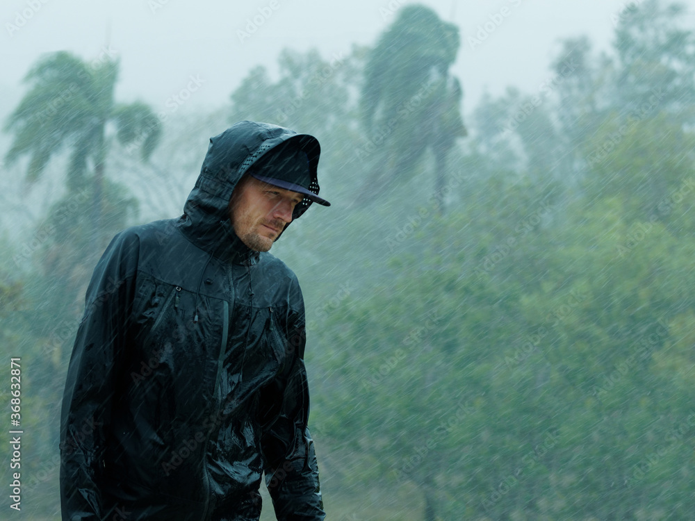 Man in raincoat under heavy tropical rain.