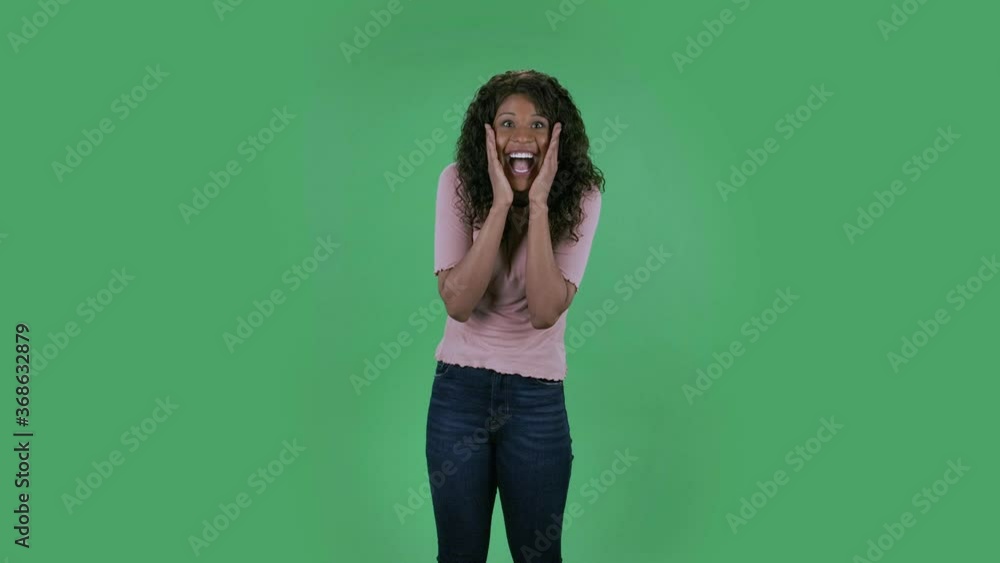 Portrait of beautiful african american young woman is looking at camera with shocked and surprised wow face expression. Burning brunette with wavy hair in jeans and a beige blouse on a green screen in Portrait of beautiful african american young woman is looking at camera with shocked and surprised wow face expression. Burning brunette with wavy hair in jeans and a beige blouse on a green screen in
