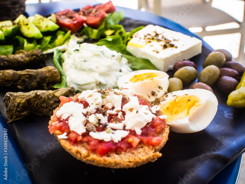 Crete plate - fresh Greek salad, feta cheese, dolmades, tomatoes, lettuce, boiled egg, black and green olives on black plate